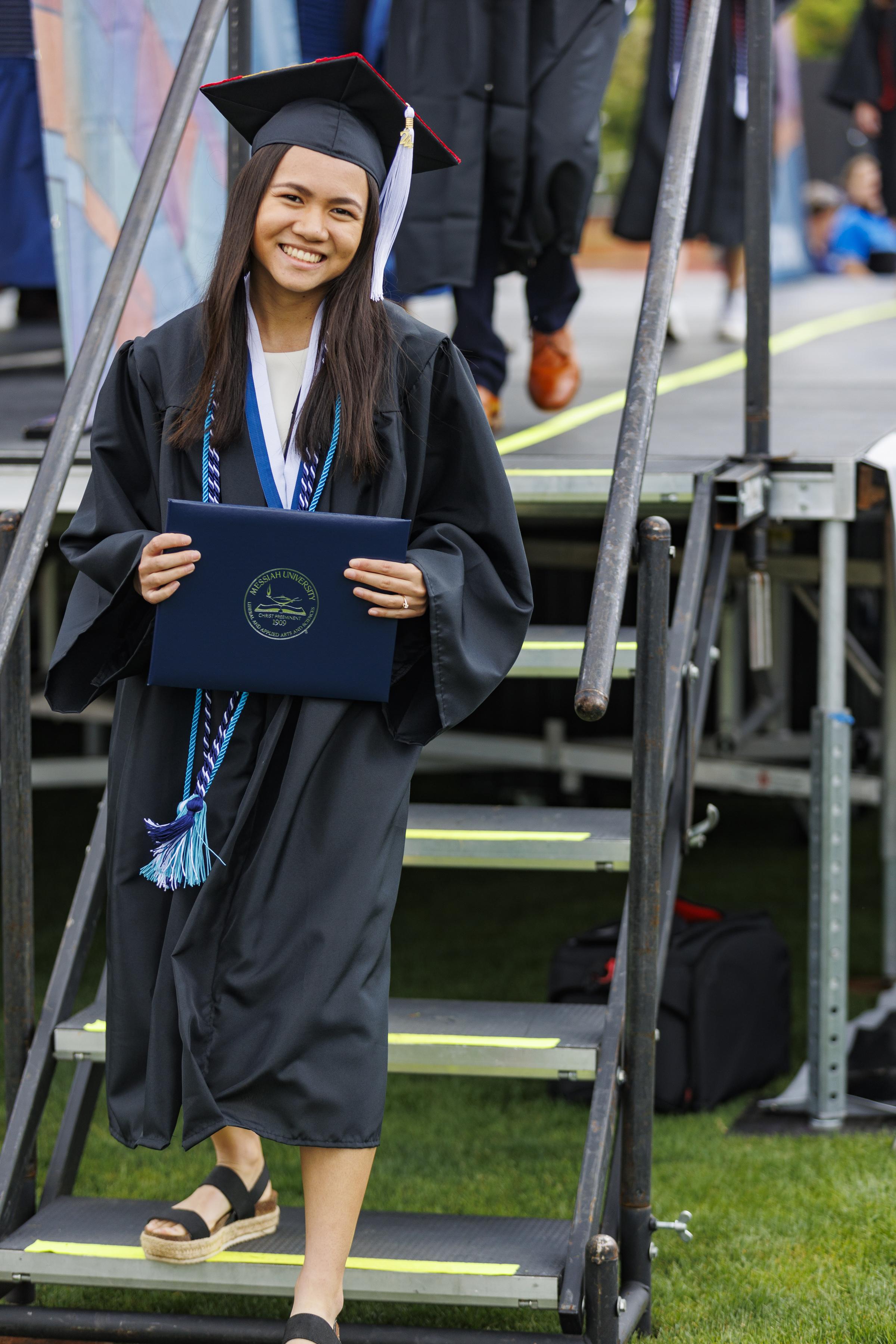 Female graduate exiting stage holding her diploma