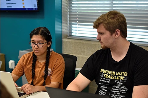 A male and female student working together at laptops at Cyber Camp