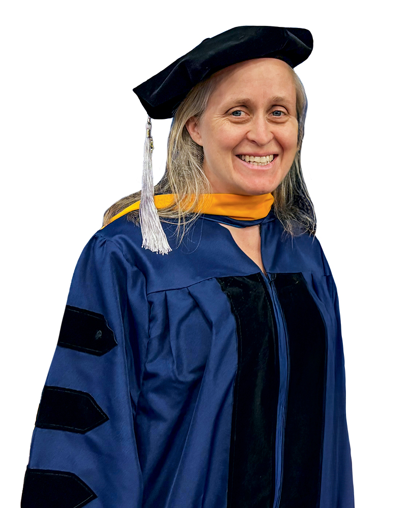 A smiling woman wearing a doctoral gown and cap, symbolizing academic achievement.