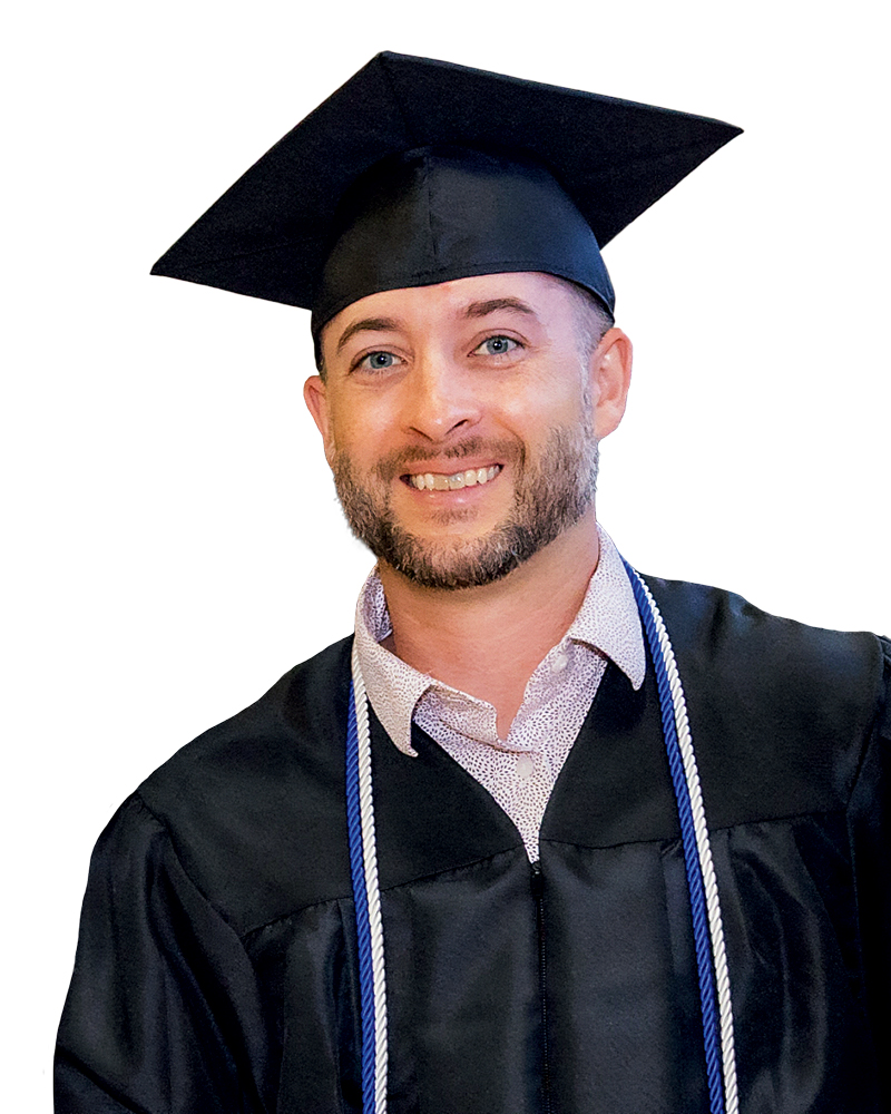 A smiling male graduate wearing a black cap and gown, with a light-colored shirt underneath and graduation cords draped around his neck.
